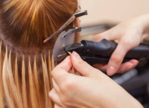 The hairdresser does hair extensions to a young girl, a blonde in a beauty salon. Professional hair care.